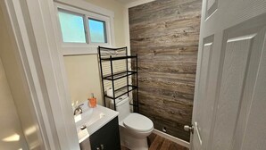 A compact bathroom with a white toilet, a black metal shelf, a white sink, and a wooden wall. - Gorgeous Cottage with Stunning Sights in Wellston, Michigan (Wellston)