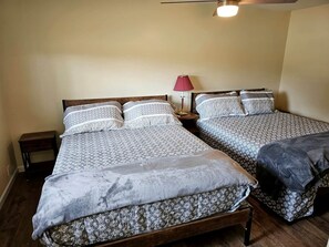 A room with two beds, a nightstand, a lamp, and a wooden floor. - Gorgeous Cottage with Stunning Sights in Wellston, Michigan (Wellston)