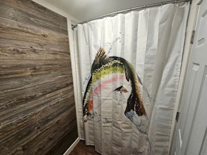 A bathroom with a wooden wall, a white shower curtain with a fish design, and a white door. - Gorgeous Cottage with Stunning Sights in Wellston, Michigan (Wellston)