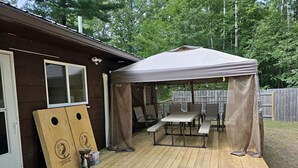 A wooden deck with a covered picnic table and chairs, a wooden playhouse, and a wooden fence. - Gorgeous Cottage with Stunning Sights in Wellston, Michigan (Wellston)