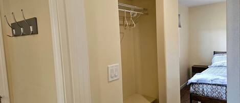 A bedroom with a bed, a closet with hanging space, and a small bedside table.
