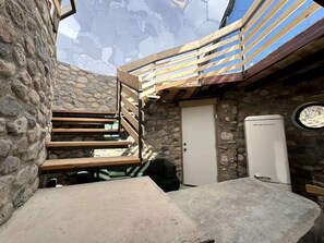 A stone-walled room with a wooden staircase, a door, and a white appliance.