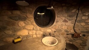 Ein Badezimmer mit Steinwänden, einem runden Spiegel, einem Waschbecken und einer Toilette.