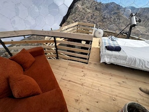 Eine Holzterrasse mit einer Couch, einem Bett und einem Teleskop.