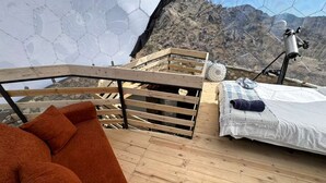 Eine Holzterrasse mit einer Couch, einem Bett und einem Teleskop.