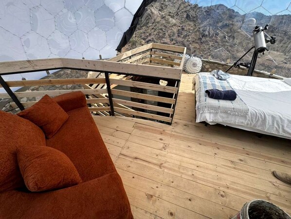 A wooden deck with a sofa, a bed, and a telescope.