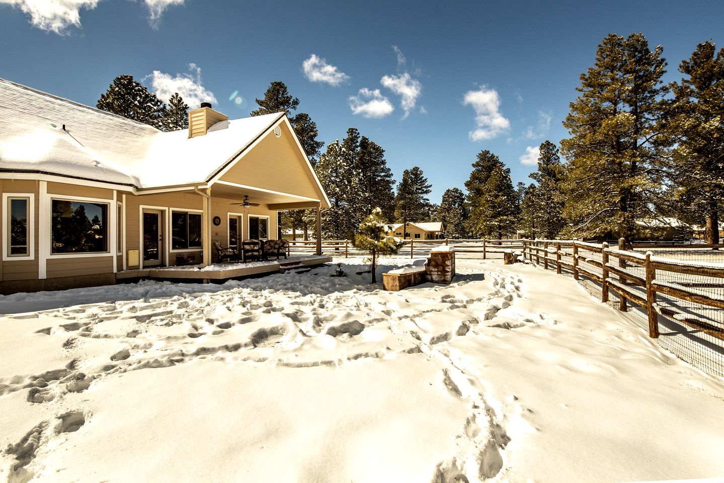 Una casa con porche cubierto, un área exterior cercada y terreno cubierto de nieve.