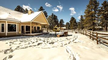Una casa con porche cubierto, un área exterior cercada y terreno cubierto de nieve.