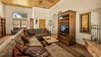 Un amplio salón con un sofá modular grande, un mueble de entretenimiento de madera y un ventilador de techo.