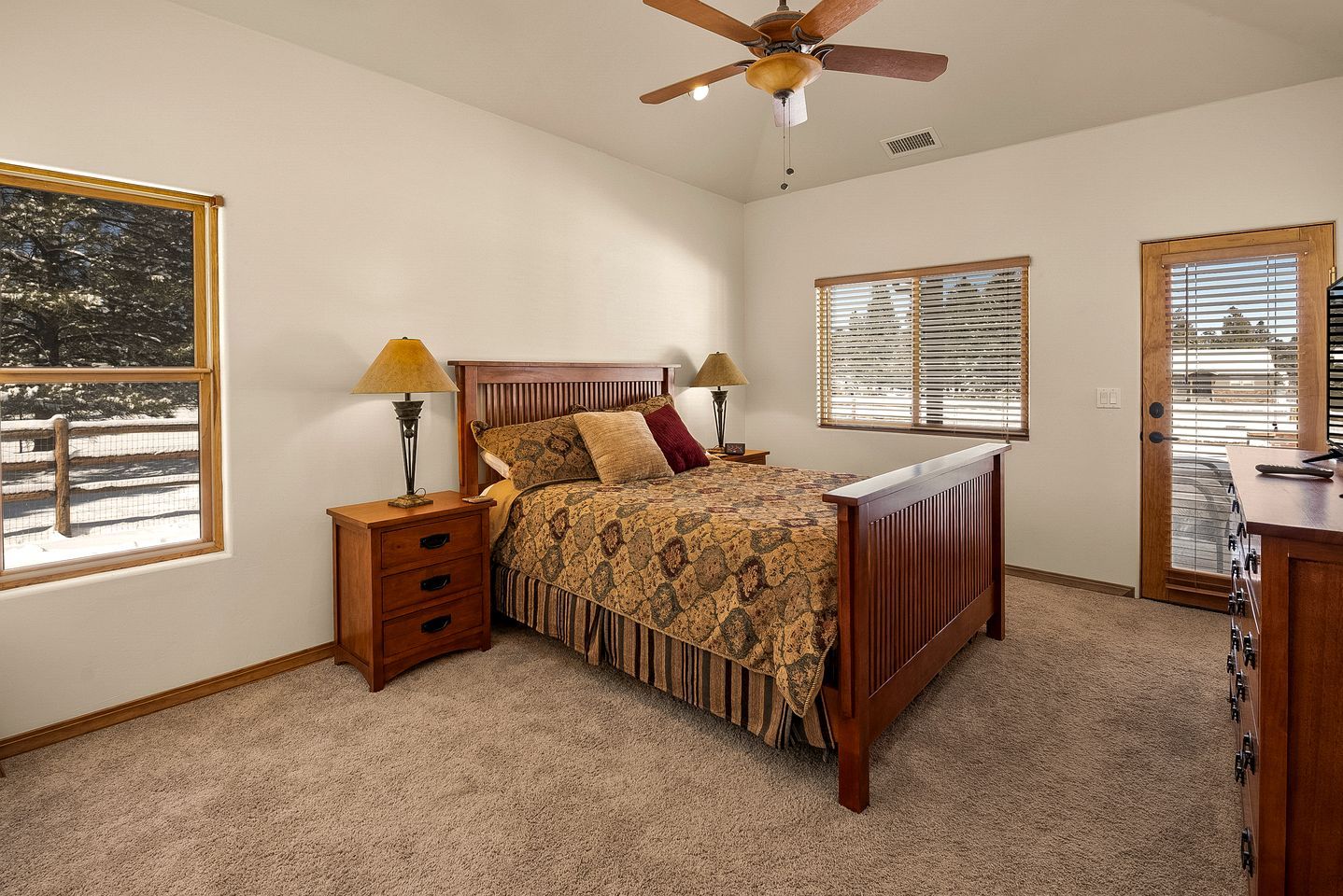 A bedroom with a bed, nightstands, a ceiling fan, and a door with a view.