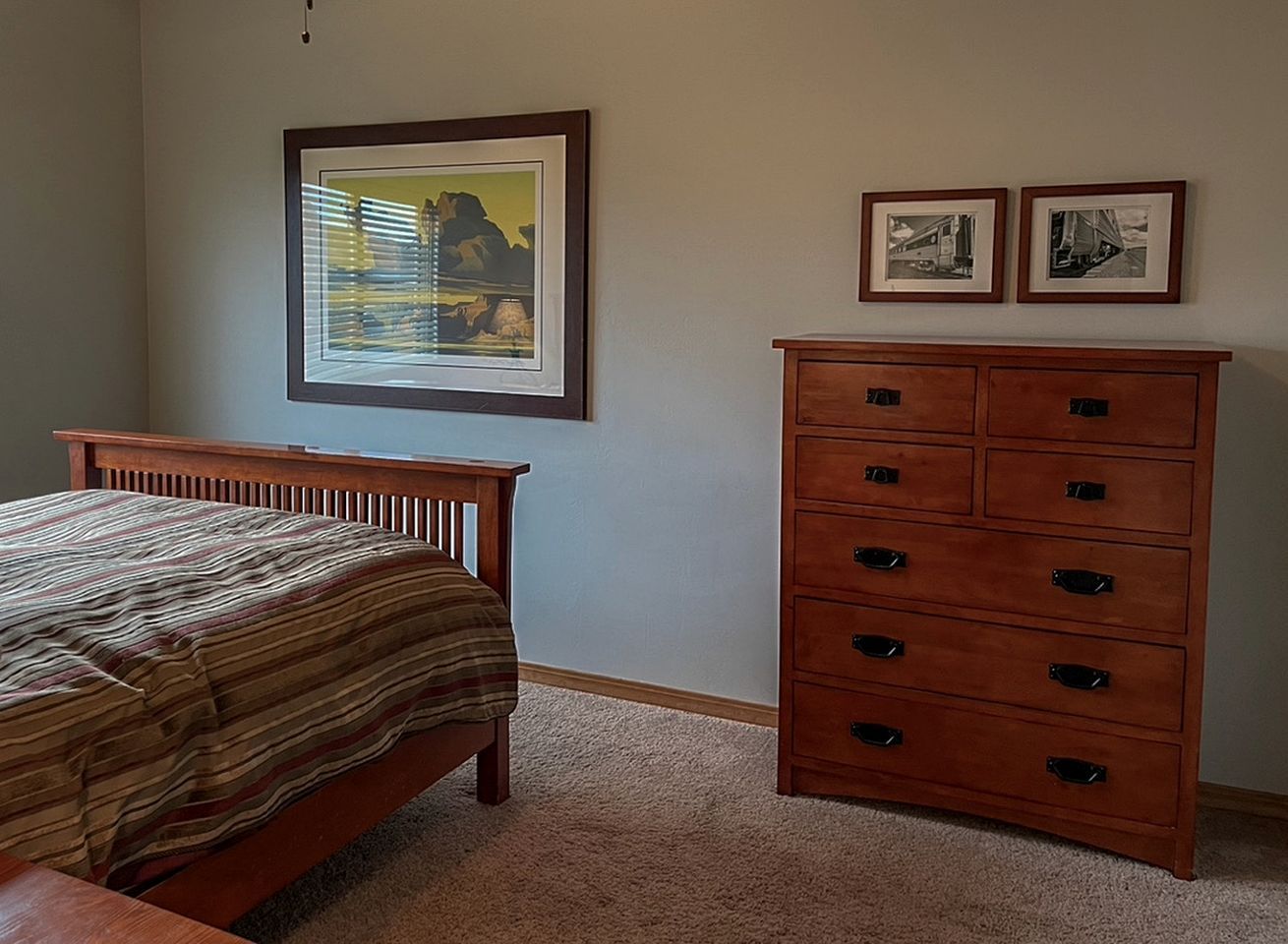 Un dormitorio con una cama, un aparador y dos cuadros en la pared.