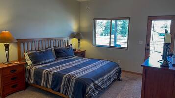Un dormitorio con una cama, dos mesitas de noche, una lámpara auxiliar y un ventilador de techo, junto con una ventana con persianas.