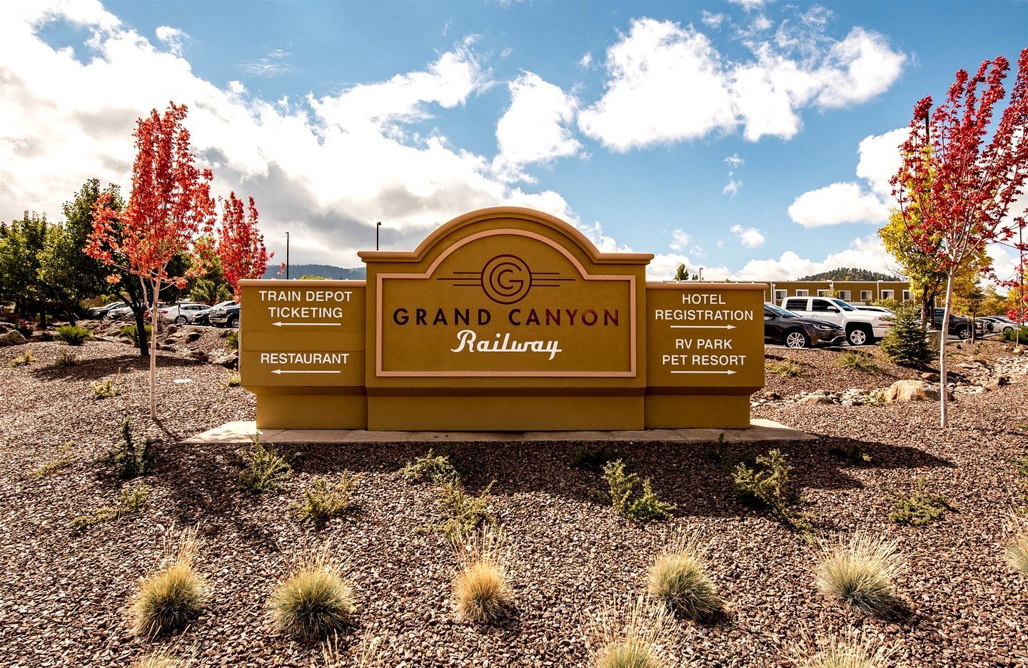Señal del Gran Cañón Railway con indicaciones hacia el depósito de trenes, venta de boletos, restaurante, registro de hotel, parque para vehículos recreativos y centro para mascotas.
