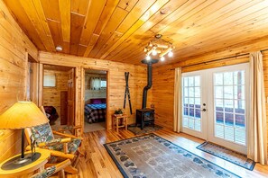 A log cabin interior with a wooden ceiling, a fireplace, a bed, a dining area, and a large window. - Pet-Friendly Log Cabin Retreat in Ely for Magical Minnesota Family Vacations (Ely)