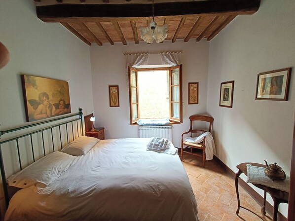 A bedroom with a bed, a chair, a table with a teapot, and a window with curtains. - Renaissance house within the historic center of Pienza (Pienza)