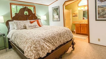 A bedroom with a wooden bed, a nightstand, a lamp, a framed picture, and a doorway leading to a bathroom.