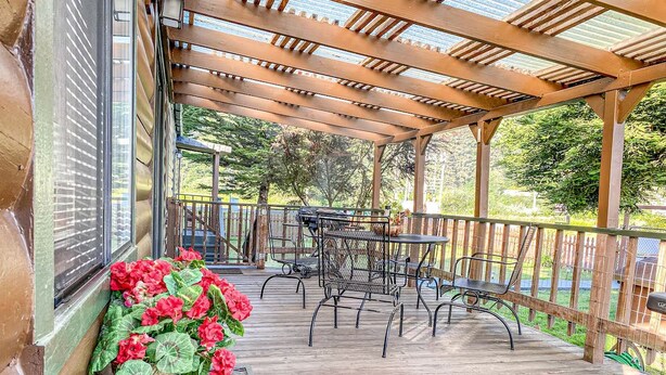 A covered outdoor patio with wooden flooring, metal chairs, and a table.