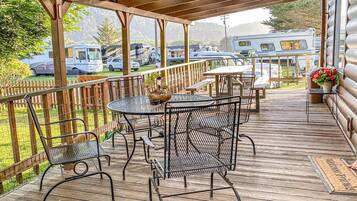 Een overdekt terras buiten met metalen stoelen en tafels, een houten hek en een uitzicht op campers op de achtergrond.
