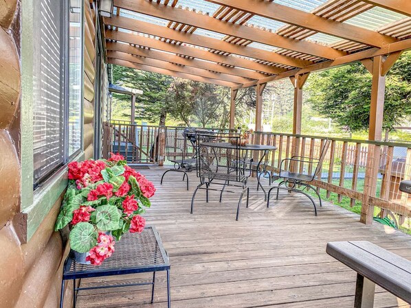 A covered outdoor patio with wooden flooring, metal chairs, and a table.