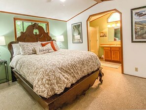 A bedroom with a wooden bed, a nightstand, a lamp, a framed picture, and a doorway leading to a bathroom.