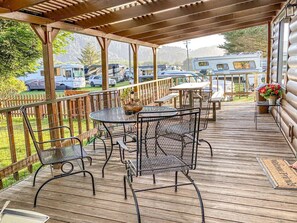 A covered outdoor deck with metal chairs and tables, a wooden fence, and a view of RVs in the background.