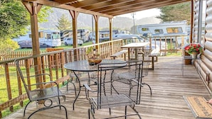 A covered outdoor deck with metal chairs and tables, a wooden fence, and a view of RVs in the background.