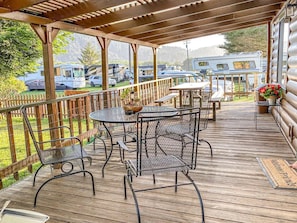 A covered outdoor deck with metal chairs and tables, a wooden fence, and a view of RVs in the background.