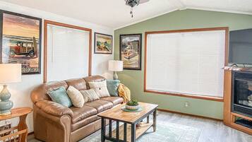 A living room with a brown leather sofa, a wooden coffee table, a ceiling fan, and framed pictures on the walls.