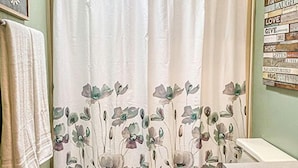 A bathroom with a shower curtain, toilet, sink, patterned rug, and motivational wall art.