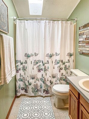 A bathroom with a shower curtain, toilet, sink, patterned rug, and motivational wall art.