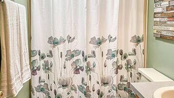 A bathroom with a shower curtain, toilet, sink, patterned rug, and motivational wall art.