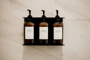 Three bottles of personal care products on a black shelf against a tiled wall. - Cute Safari Tent for Two in Erwin, Tennessee (Erwin)