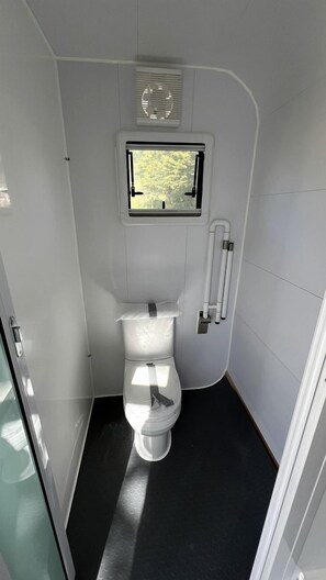 A compact, white bathroom with a toilet, a small window, and a vent.