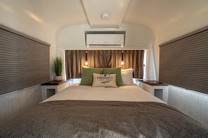Ein Schlafzimmer mit Bett, Nachttisch, Topfpflanze, Kissen mit Aufdruck und Klimaanlage.