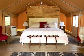 A tent-style room with a bed, two chairs, a radiator, and a lamp.