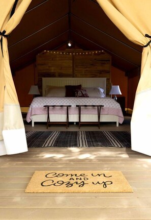 A cozy bedroom with a bed, bedside tables, a bedside lamp, a rug, and a welcome mat.