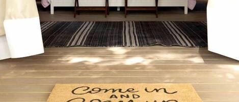 A cozy bedroom with a bed, bedside tables, a bedside lamp, a rug, and a welcome mat.