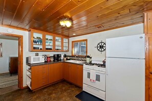 Eine kleine Küche mit Holzschränken, einem weißen Kühlschrank, einem Herd und einer Mikrowelle.