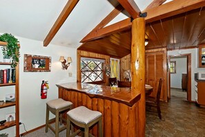 A wooden interior with a bar area, stools, a bookshelf, and a fire extinguisher. - Forest Cottage with Outdoor Jacuzzi and Picnic Space in California (Big Bear Lake)