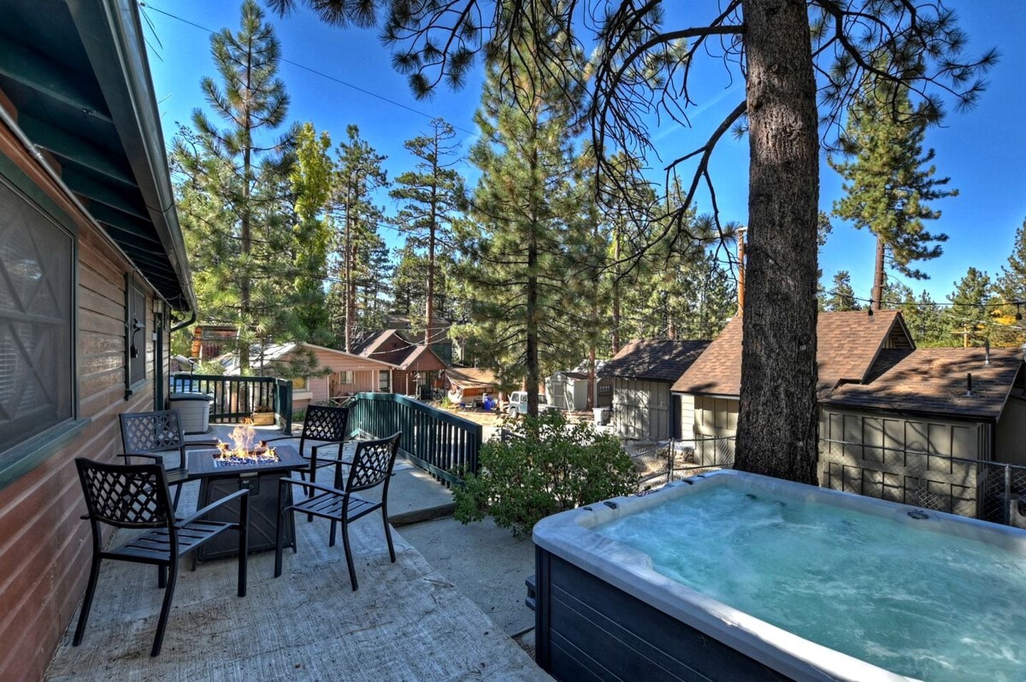 A hot tub on a patio with a view of a forested area and neighboring houses.