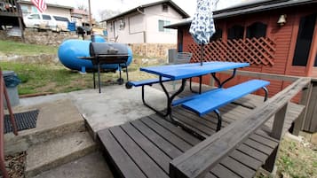A wooden picnic table with benches, a barbecue grill, and a covered umbrella.