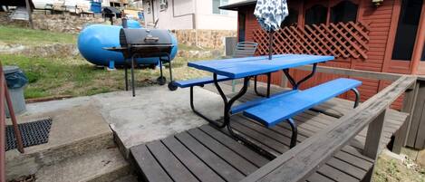 A wooden picnic table with benches, a barbecue grill, and a covered umbrella.