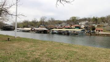 A riverside view with docked boats, a grassy bank, and residential buildings in the background.