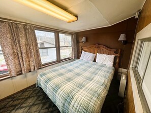Une chambre à coucher avec un lit, une fenêtre avec des rideaux, une lampe fixée au mur et un radiateur.