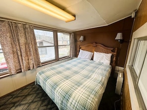 Un dormitorio con cama, ventana con cortinas, lámpara de pared y radiador.