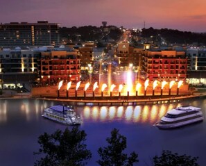 A waterfront hotel with a central fountain, boats docked, and surrounding buildings.