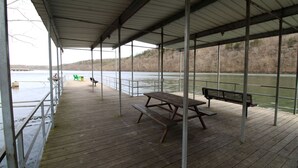 Eine überdachte Holzterrasse mit Picknicktisch und Bänken, mit Blick auf ein Gewässer.