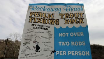 Skilt for Rockaway Beach Public Trout Fishing Dock med en liste over fisketilladelser og reglen om højst to fiskestænger per person.