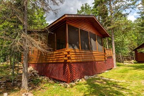 Eine Blockhütte mit einer Terrasse, umgeben von Bäumen.