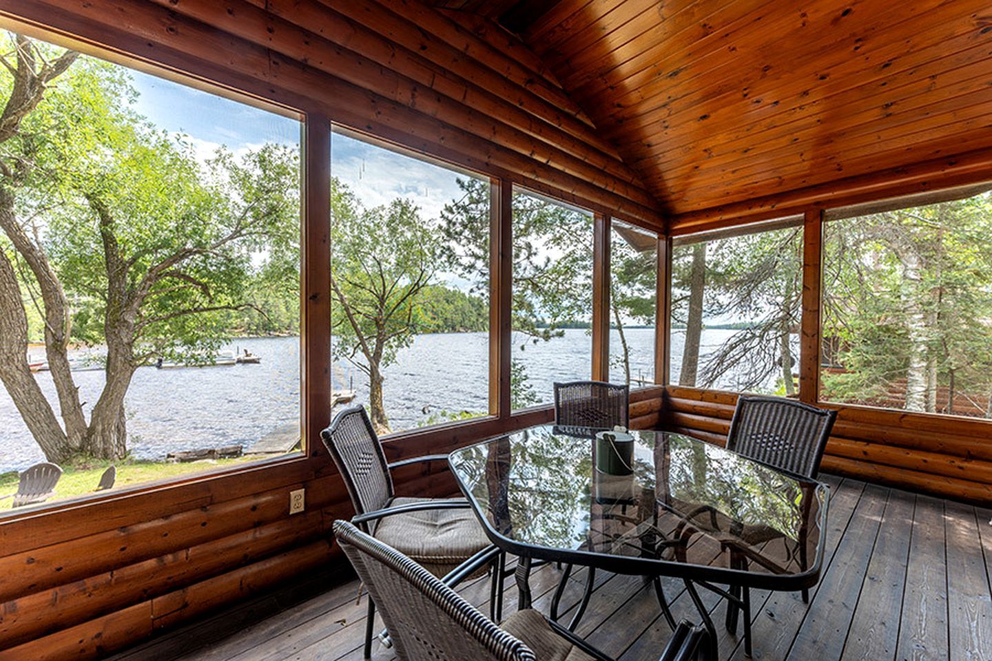 A wooden cabin with a glass table and chairs, overlooking a lake.
